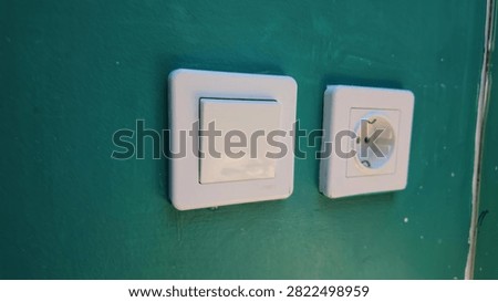 A white electrical light switch and a matching power outlet socket installed on a green wall.