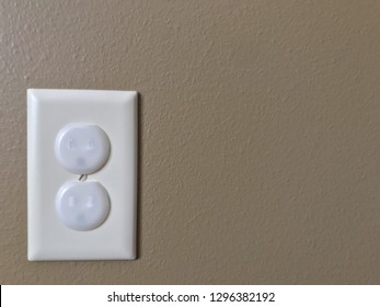 White Electrical Outlet With Baby Proof Covers Against Tan Drywall 