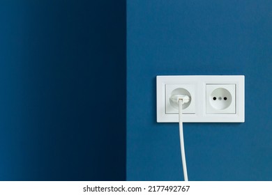 White electrical plug in the electric double socket on a blue wall