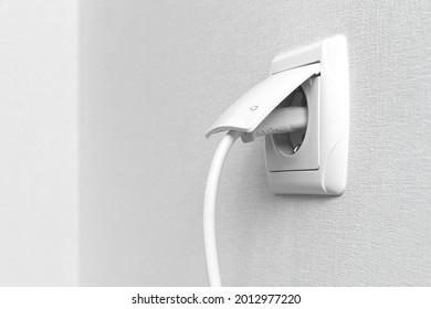 White electrical plug in the electric socket on a wall, interior 