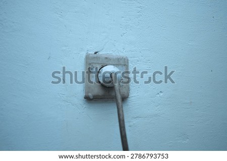 A white electrical power plug inserted into a vintage and dirty wall outlet against a light blue textured wall.