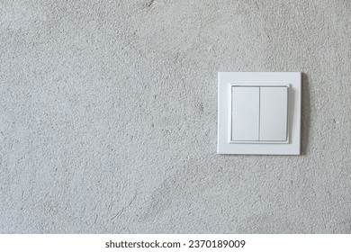 White electrical switch on a gray unfinished wall with plaster. Close-up. Form. Background.