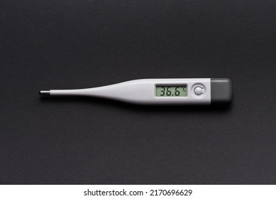 White Electronic Thermometer Shows Normal Body Temperature On A Black Background