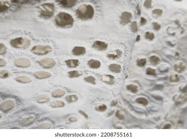 White embroidered fabric with a floral print of small round holes, in diagonal folds (macro, top view, texture). - Shutterstock ID 2208755161