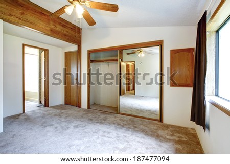 White empty bedroom with mirror door closet, blade ceiling fan and carpet floor