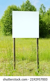 A White Empty Billboard In The Forest Among The Trees. Posting Information In A Public Park Or Drawing Attention To Environmental Issues. Summer, Copy Space.