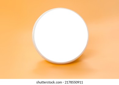 A white empty blank round plastic container stands on an orange background. Mock. Circular. Nutrition. Can. Pack. Packing. White. Butter. Design. Cover. Closed. Shape. Cheese. Small