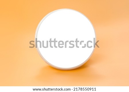A white empty blank round plastic container stands on an orange background. Mock. Circular. Nutrition. Can. Pack. Packing. White. Butter. Design. Cover. Closed. Shape. Cheese. Small