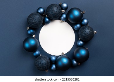 White empty circle with frame of blue matte and glitter Christmas ornaments on dark blue background with copy space
