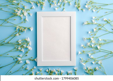 White empty photo frame mockup with mouse-ear chickweed flowers on blue background, top view copy space