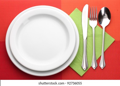 White Empty Plate With Fork, Spoon And Knife On A Red Tablecloth