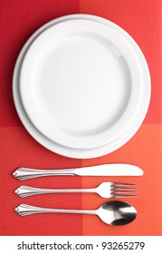 White Empty Plate With Fork, Spoon And Knife On A Red Tablecloth