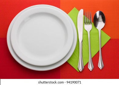 White Empty Plate With Fork, Spoon And Knife On A Red Tablecloth