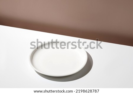 White empty plate on white table. Blank, still life scene, beige wall, background with plate. Minimal mockup for food. Design Template. Front diagonal view.