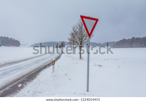 White empty snowy icy winter road track with yield\
sign. The street track is slick and frozen. High dangerous risk of\
an accident through blizzard snowstorm in severe weather christmas\
season