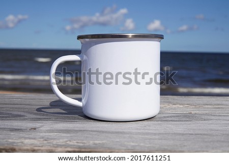 White enamel mug mockup for design presentation, close up blank camping cup on outdoor camping, the sea on background.
