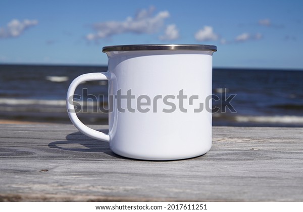 White\
enamel mug mockup for design presentation, close up blank camping\
cup on outdoor camping, the sea on\
background.
