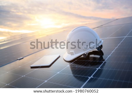 White engineer hard hat and a tablet placed on the solar panel At a photovoltaic power station working on solar energy storage in the industry.
