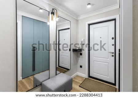 White entrance door in a modern renovated hallway with large mirrors and wardrobe.