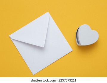 White envelope with a heart-shaped gift box on yellow background. Valentine's day concept