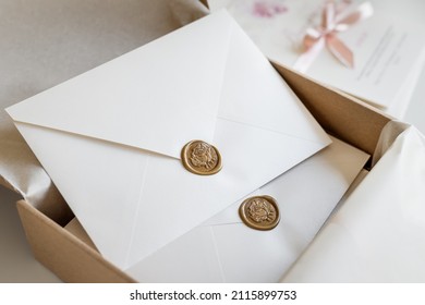 White envelopes sealed with golden floral wax stamp, luxury stationery packed in a box and ready to mail