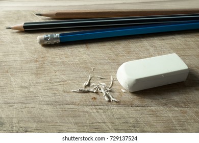 White eraser and eraser dust on old wooden background with three pencil,mistake concept