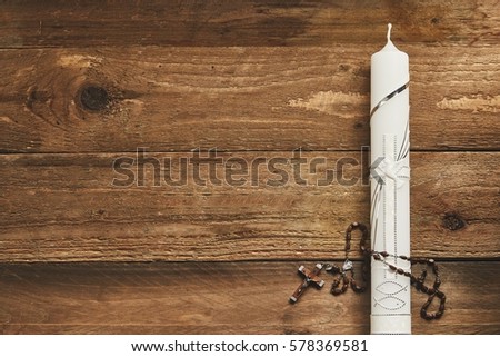 White Eucharist candle decorated with a silver cross and rosary on a rustic wood background with copy space, conceptual of communion and Easter