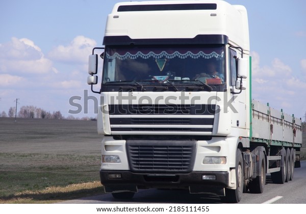 White Euro semi truck with empty lowbed trailer on\
country road front view