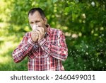 A white European man sneezes and blows his nose into a paper napkin against a green background. Spring exacerbation of allergy to poplar fluff. Allergy in adults hay fever