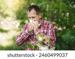 A white European man sneezes and blows his nose into a paper napkin against a green background. Spring exacerbation of allergy to poplar fluff. Allergy in adults hay fever