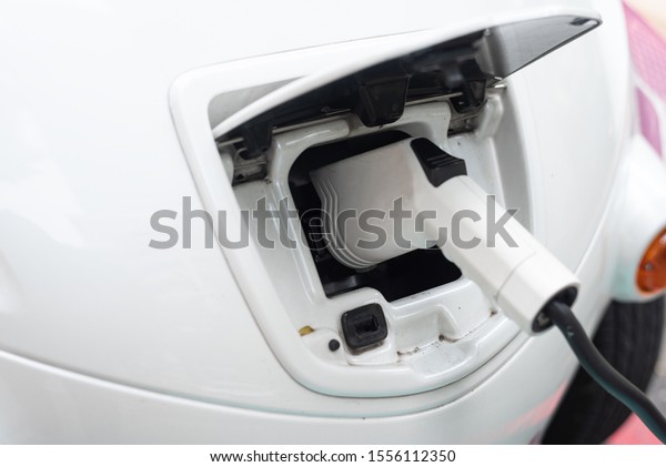 White EV Car or Electric car at charging\
station,plugged in for charging. Close up of the power supply\
plugged into an electric car being\
charged