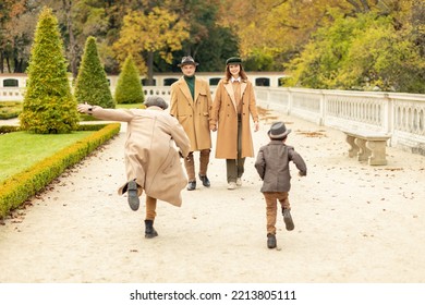 White Excited Children (kids,two Brothers) Running Towards Parents Into Arms,having Fun Walk In Autumn Park, Wear Beige Warm Coats (jackets),boots, Hats. Stylish Happy Family.Fall Season. Horizontal