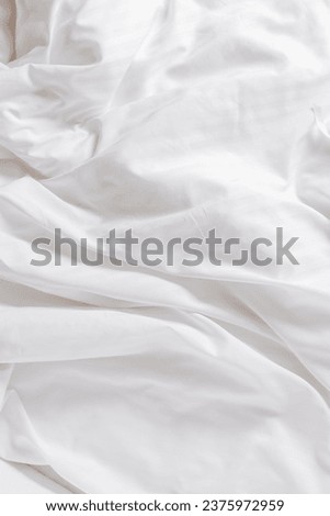 White fabric texture background, wavy cloth. Crease bedclothes fragment as background, Crumpled sheet of bed. White bed linen as minimal backdrop. Top view aesthetic surface, vertical screensaver
