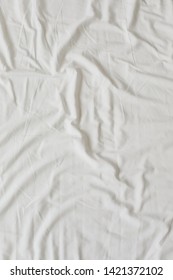 White Fabric Texture Background. Wrinkled, Crumpled Fabric. Top View Of A Messy Bedding Sheet After Night Sleep. Unmade Bed Sheet In The Bedroom After Night Sleep. Soft Focus