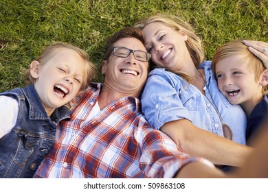 White family lies on grass taking selfie, camera out of shot - Powered by Shutterstock