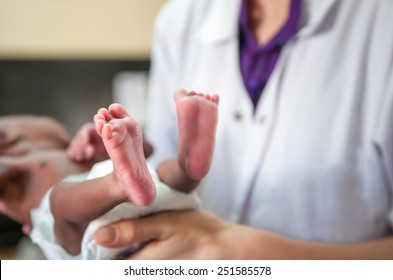 White female doctor or nurse is holding small infant. Baby's foot is in focus.