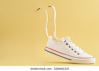 White female sport sneakers with flying shoe lace against yellow background, Casual trendy shoes closeup, Creative minimal design with copy space