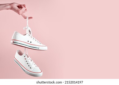 White female sport sneakers hanging on woman hand with shoe lace against pink background, Casual trendy shoes closeup, Creative minimal design with copy space - Shutterstock ID 2152014197