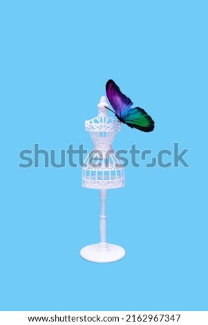 The white female tailor doll with a butterfly on the shoulder isolated against a pastel blue background. Minimal fashion concept