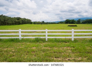 White Fence In Farm Field And Overcast Sky