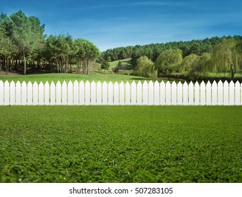 White fences on green grass and the trees behind