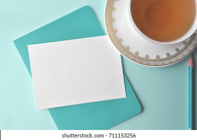 White Fine China Cup Of Tea With A Blank Note Card And Teal Book On Mint Background