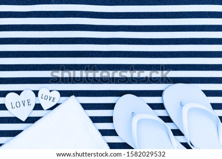 White flip flops shoes and towel on trendy blue white striped beach mat background, top view, copy space. White Toe sandals, flat lay, text place. Summer background with flipflop shoes, flatlay. 