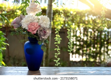 White flowers Blossoms in a Crazed Blue Vase on a Table Outdoors with Green in the Background with Copy Space  for your Text. image