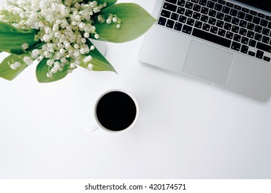 White flowers, laptop and a coffee cup on a white background. Styled photo. Feminine scene.