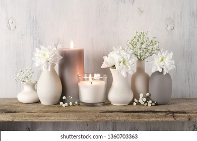 White Flowers In Neutral Colored Vases And Burned Candles On Rustic Wooden Shelf Against Shabby White Wall. Home Decor.