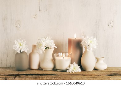 White Flowers In Neutral Colored Vases And Burned Candles On Rustic Wooden Shelf Against Shabby White Wall. Home Decor.