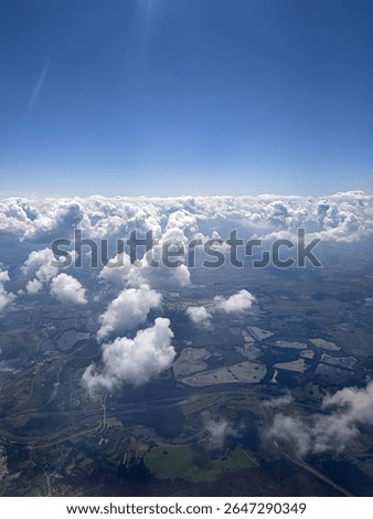 White fluffy clouds floating above patchwork fields, viewed from high altitude during a plane journey.