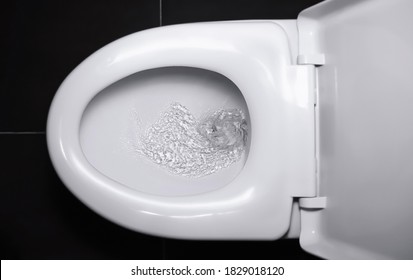 The white flush toilet bowl that the water is draining. concept of flushing away something. - Shutterstock ID 1829018120