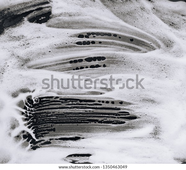 White foam and soap on black\
background. Abstract pattern. Car wash. Guest worker\
concept.